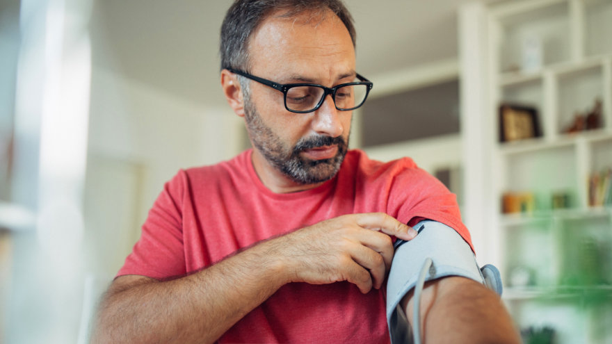 A middle-aged man in his home, operating a blood pressure sleeve to check his numbers.