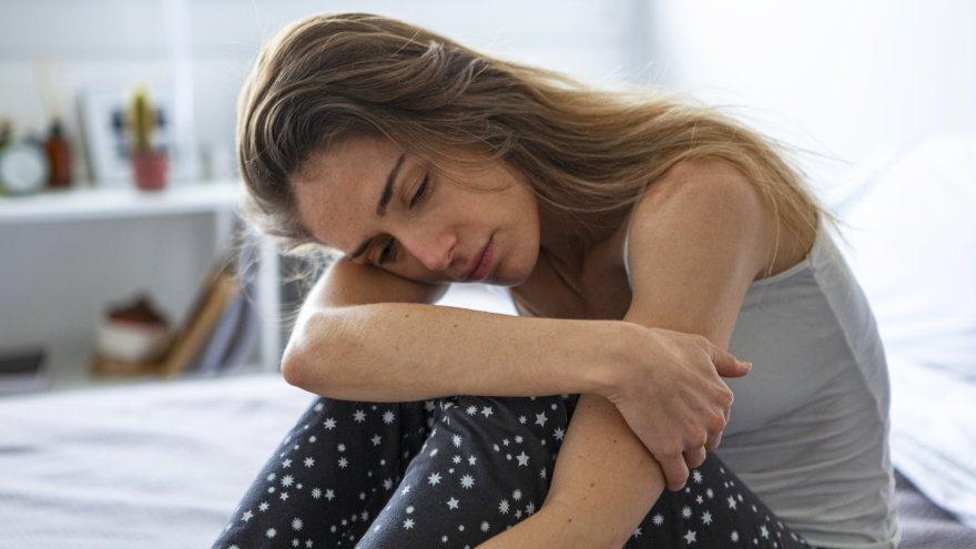 A fatigued woman sitting dejectedly on her bed in pajamas.