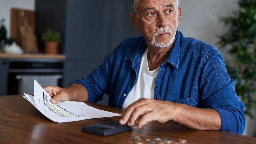 A mature man examining a medical bill at his table with a calculator in hand, look off wondering how he's going to pay for this.