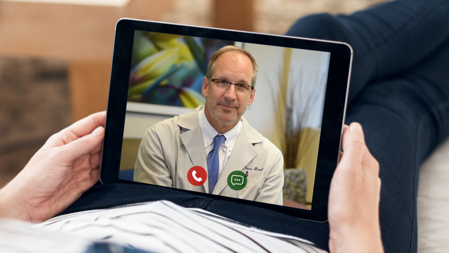 A couple sittings on the couch watching the screen of a laptop where a doctor can be seen.