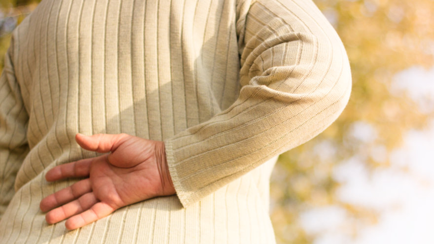 Woman gingerly placing the back of her right hand on the small of her back.