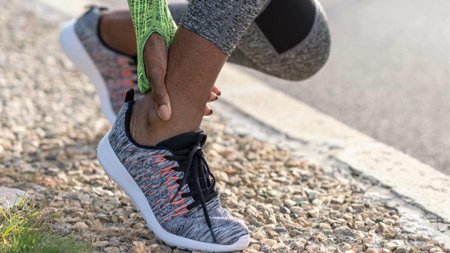 Woman in active wear bending over and holding her ankle, possibly in pain.