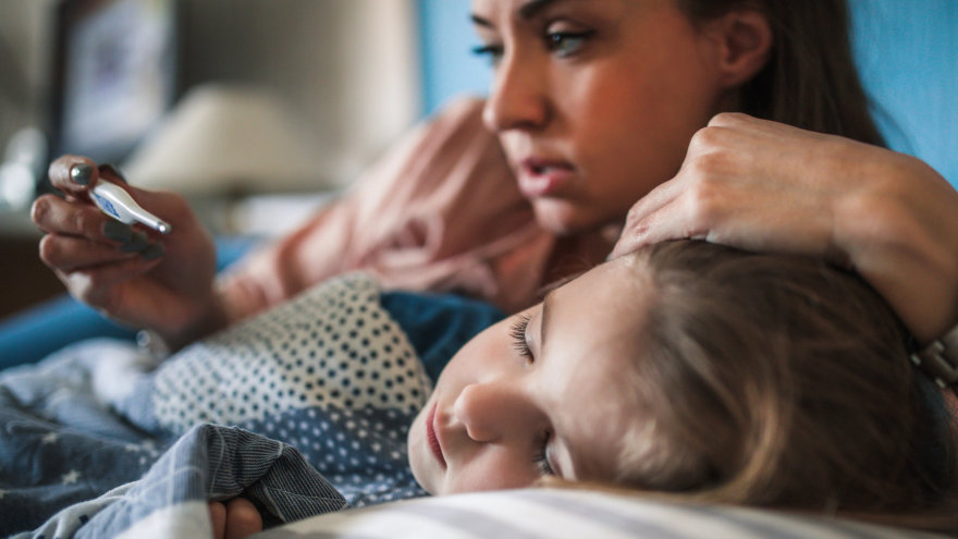 A mother taking the temperature of her sick, sleeping child.