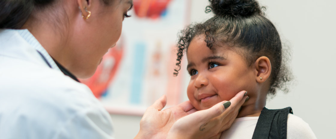 A physician affectionately cradling the face of her young patient who is smiling up at her.